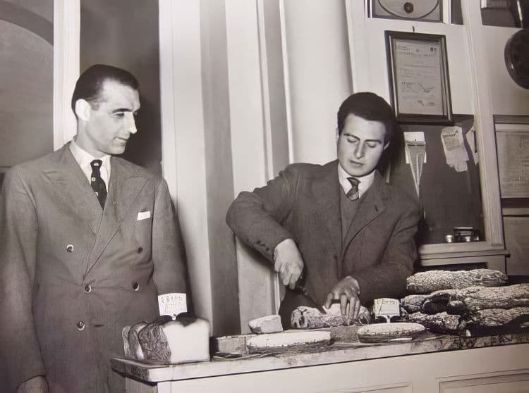 The Mattei shop, mid/late 1950s From left: Olimpio Pandolfini and Renzo Guarducci slicing a piece of Glac&egrave; Cherry Loaf. On the right, a stack of candied loaves.